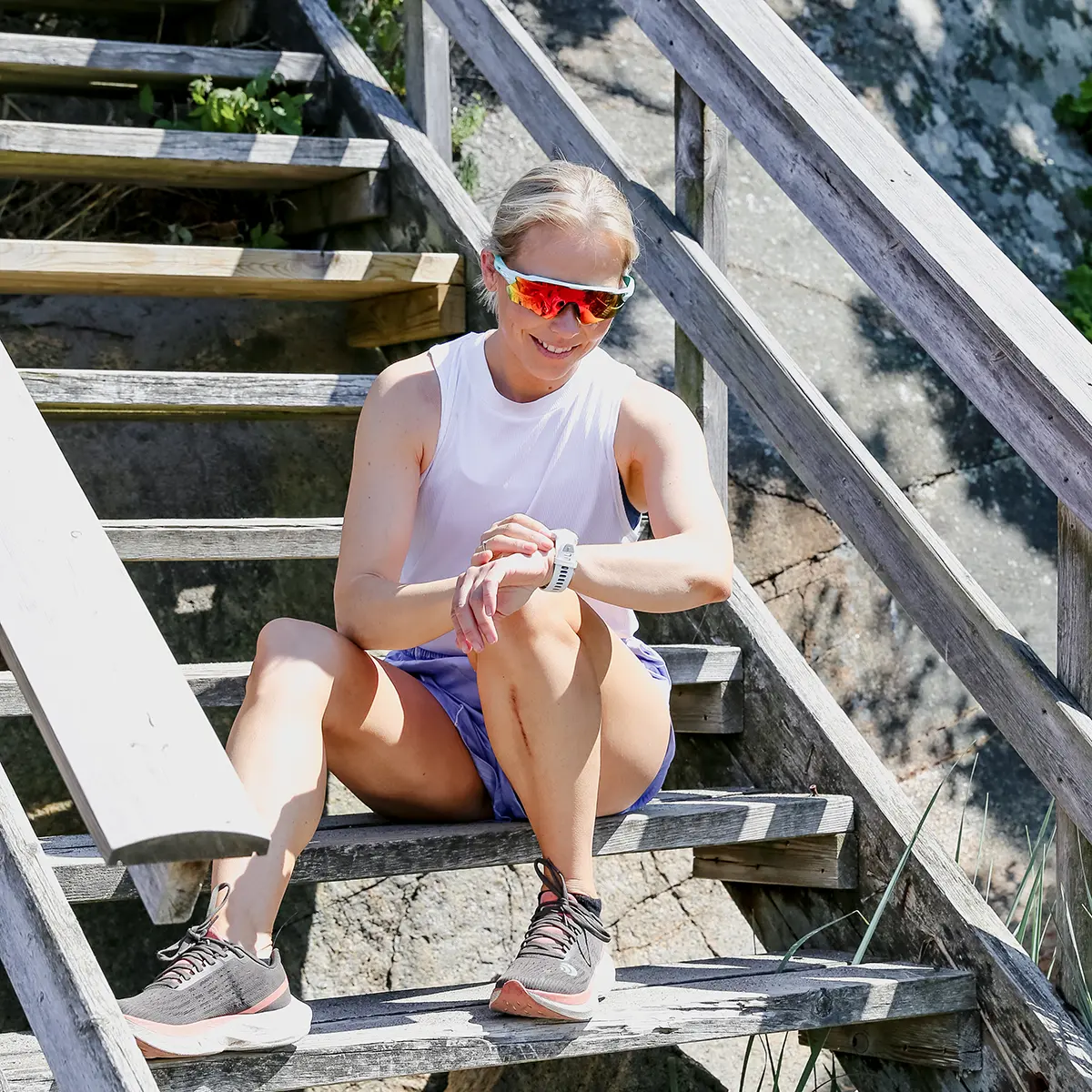 Løpetrener Desiree sitter på en trapp med solbriller og viser sitt online løpe- og styrkeprogram Sterkere Løper